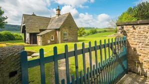 A stone house with a sloped roof and a wooden fence. - Russian Cottage Chatsworth Estate (Edensor)