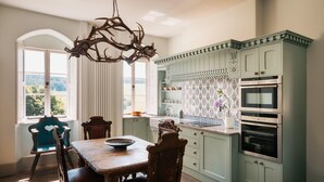 A kitchen with a dining table, chairs, a chandelier, and a view of the outdoors. - Russian Cottage Chatsworth Estate (Edensor)