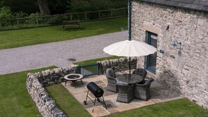 A stone building with a patio area featuring outdoor furniture, a grill, and a white umbrella. - Dipper Cottage Upperdale | Peak District (Buxton)