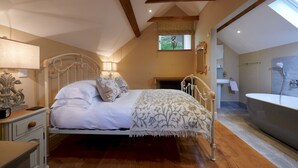 A bedroom with a bed, bedside table, lamp, and a view of the bathroom. - Dipper Cottage Upperdale | Peak District (Buxton)
