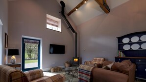 A cozy living room with a fireplace, plaid furniture, and a view through a large window. - Dipper Cottage Upperdale | Peak District (Buxton)