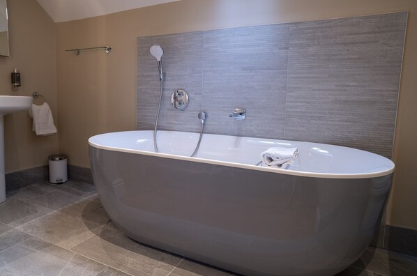 A modern bathroom with a freestanding bathtub, a wall-mounted showerhead, and a sink with a towel rack.