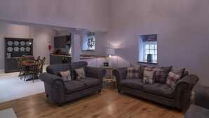 A spacious living room with two dark sofas, a wooden dining table, and a kitchen area in the background. - Kingfisher Cottage Upperdale | Peak District (Buxton)