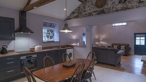 A modern kitchen with a dining area, stone wall, and a cozy living room with a sofa and armchairs. - Kingfisher Cottage Upperdale | Peak District (Buxton)