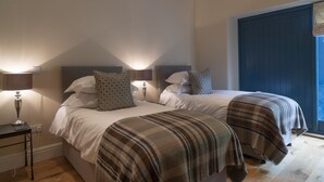 A bedroom with two beds, a nightstand, a lamp, and a window with a view. - Kingfisher Cottage Upperdale | Peak District (Buxton)