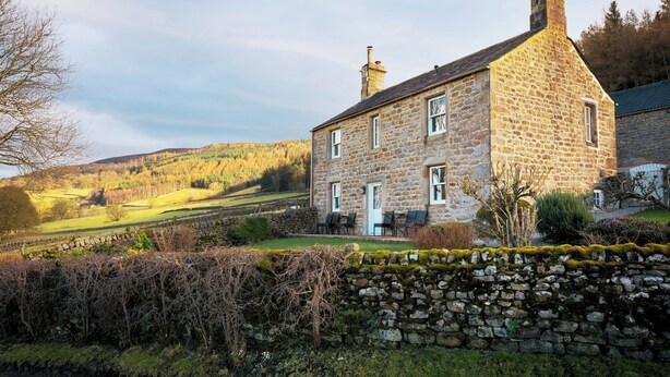 Une maison en pierre avec une cheminée, un mur en pierre et un jardin.