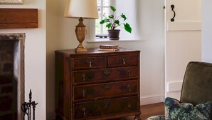Une pièce chaleureuse avec une commode en bois, un fauteuil vert, un tapis rouge et une cheminée.