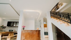 A modern kitchen with a wooden bench, a curved wooden counter, and a staircase with a black railing. - Nova Guest House (Pererenan)