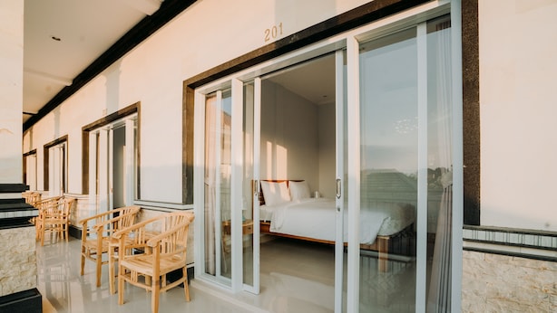 A hotel room with a bed, a desk, and chairs. There is a sliding glass door leading to the room. - Nova Guest House (Pererenan)