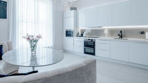 A modern kitchen with white cabinetry, a round glass table, and a vase with flowers.