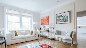 A modern living room with a white sofa, a glass coffee table, and a gold-framed armchair.