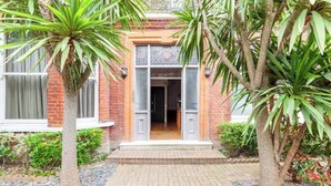 A brick building with a tiled entrance, surrounded by palm trees and a gravel pathway.