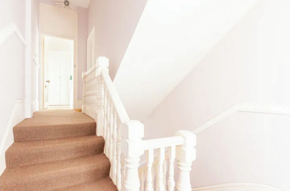 A staircase with white railings and beige carpeted steps leading to a door at the top.