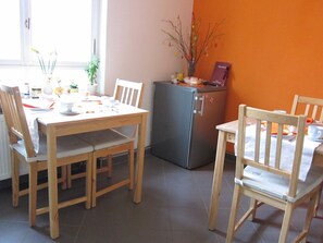Un coin repas avec une table et des chaises en bois, un réfrigérateur et un vase décoré de branches, accroché au mur.