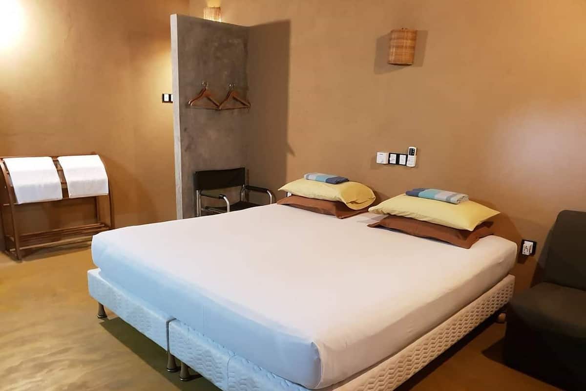 A bedroom with a large bed, a chair, a towel rack, and a small table.