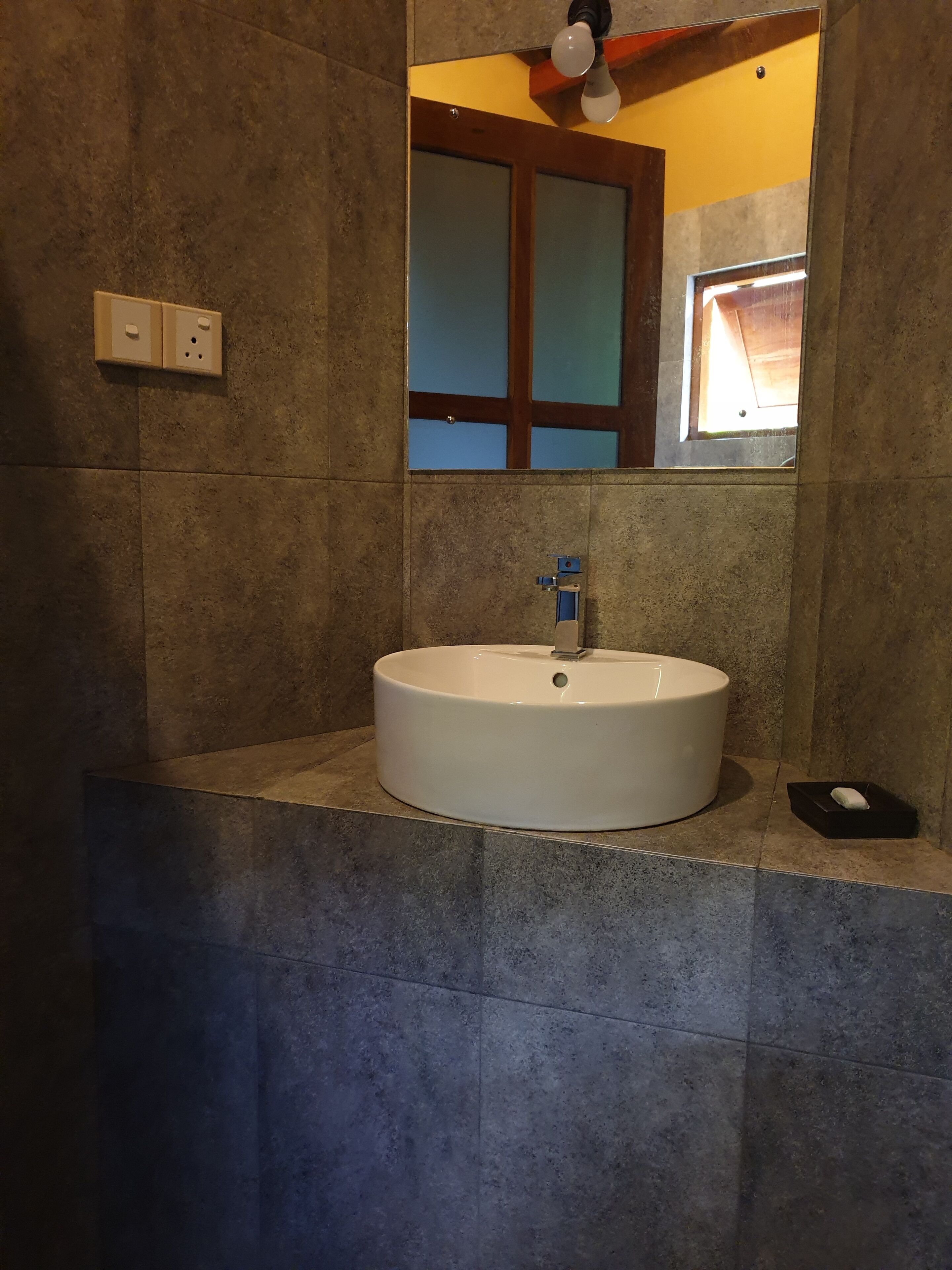 A bathroom with a white sink, a mirror, and a window.