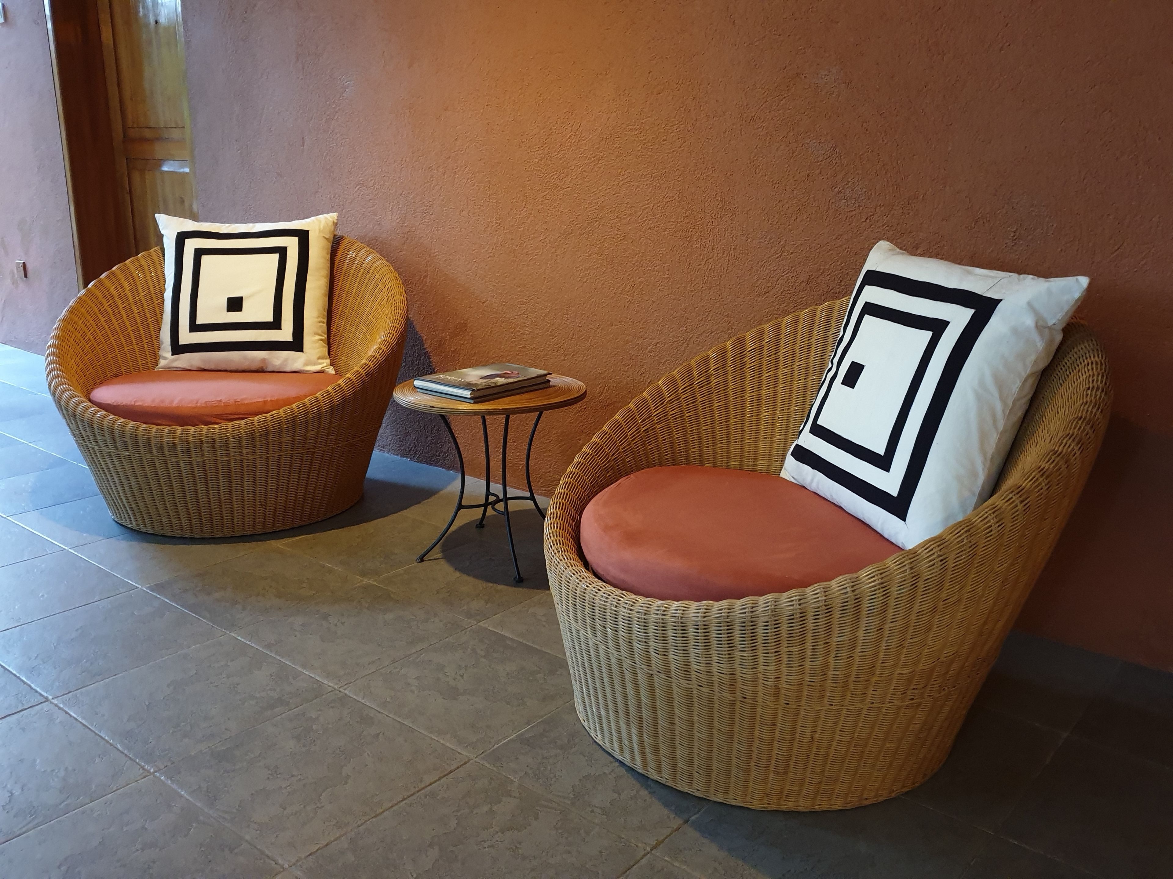 Two wicker chairs with cushions and a small table with a book, against a textured wall.