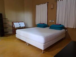 Ein Zimmer mit einem Einzelbett, einer weißen Matratze, blaustürkis-farbenen Kissen und einem Holz-Kopfende.