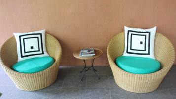 Two wicker chairs with teal cushions and black and white patterned pillows, positioned on a tiled floor with a small round table between them.