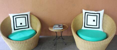 Two wicker chairs with teal cushions and black and white patterned pillows, positioned on a tiled floor with a small round table between them.