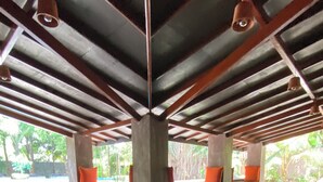 A spacious indoor area with a high ceiling, concrete pillars, and seating areas with orange cushions. - My Village (Thissamaharama)