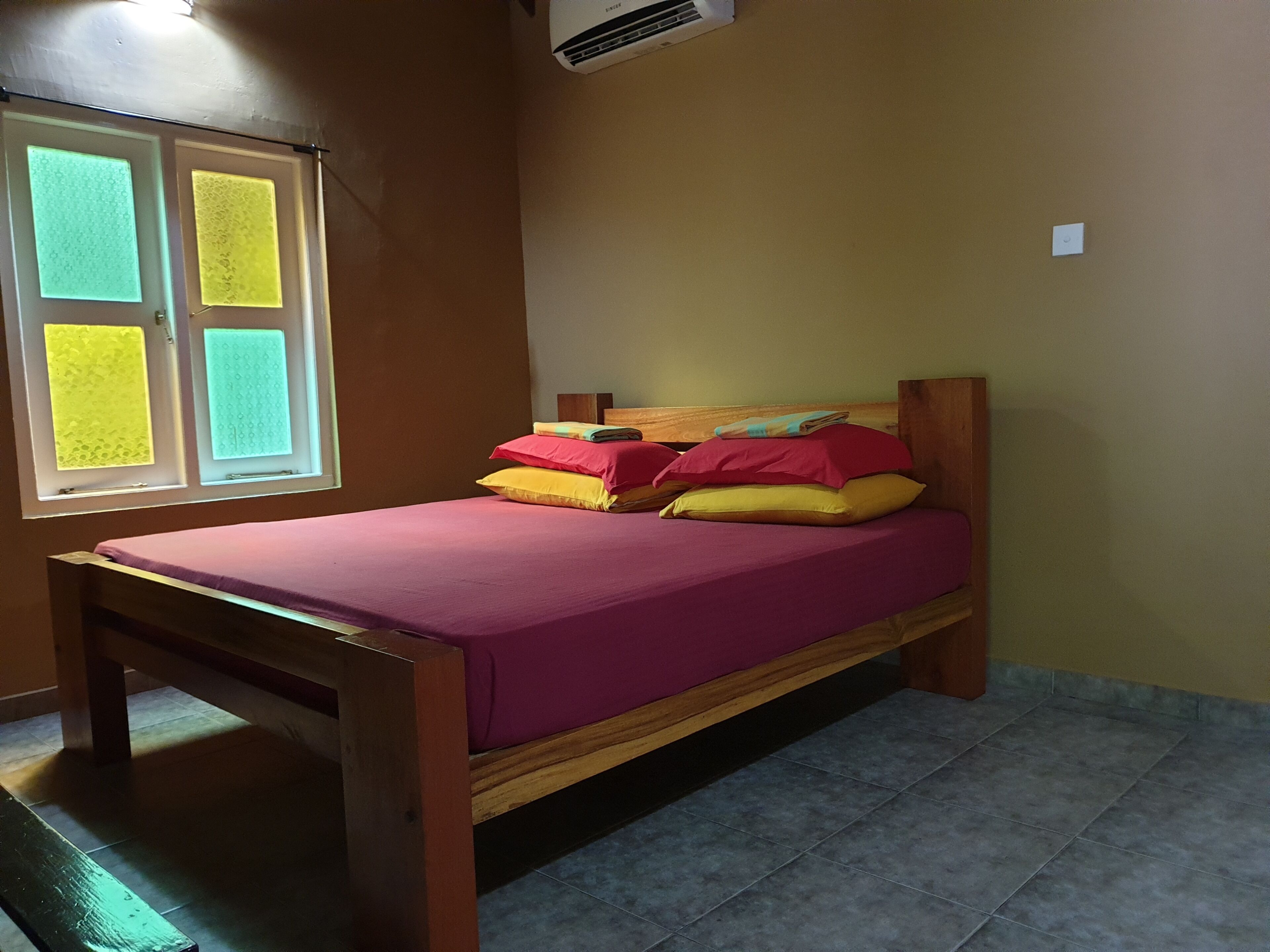A single bed with a wooden frame and a purple mattress in a room with brown walls and a window with frosted glass panels.