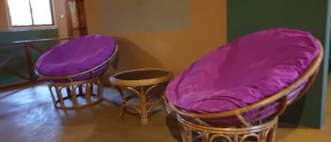 Sillas de mimbre con cojines morados en una habitación con piso de madera y pared verde.