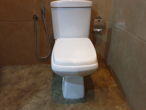 A white toilet with a shower attachment in a bathroom with brown tiled walls.
