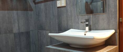 Ein modernes Badezimmer mit einem großen Waschbecken, einem Spiegel und einer Dusche.