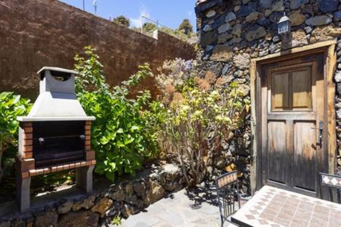 Un bâtiment en pierre avec une porte en bois et un barbecue dans le jardin.