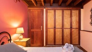 Quarto com guarda-roupa de madeira, mesa de cabeceira com abajur e cama com cobertor branco.