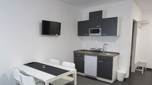 A compact kitchen with a dining table and chairs, a microwave, a dishwasher, and a TV mounted on the wall. - Hotel201 (Gablitz)