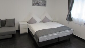 A bedroom with a bed, a bedside table, a nightstand, a couch, and a window with curtains. - Hotel201 (Gablitz)