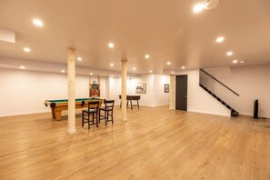 A spacious room with a pool table, chairs, and a staircase.