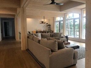 A spacious living room with a large sectional sofa, a dining area with a table and chairs, and large windows offering a view of the outdoors. - Carpe Diem Sunset View (Mactier)