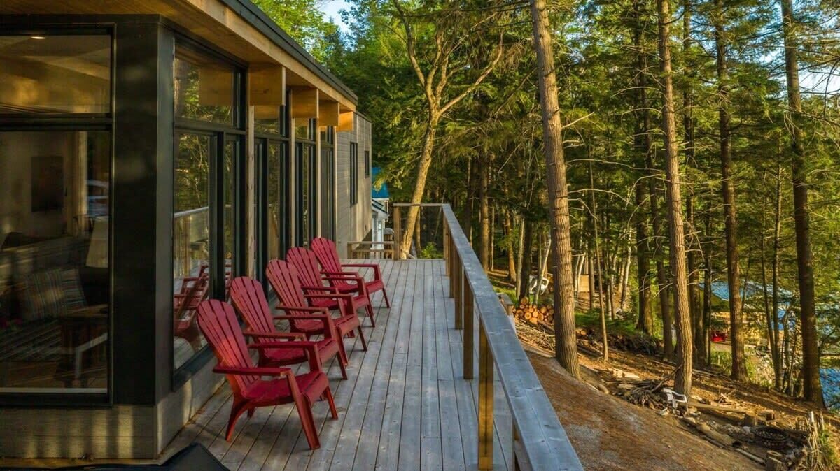A wooden deck with red chairs, overlooking a forested area.