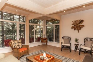 A spacious room with large windows, wicker furniture, and a decorative wall piece.