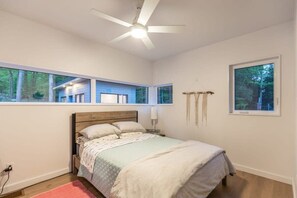 A bedroom with a bed, a ceiling fan, a window with a view of a house, and a wall-mounted light. - Carpe Diem Sunset View (Mactier)