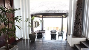 A spacious indoor area with a dark wooden floor, a sofa, two chairs, and two large planters with plants. - The Bukit Ocean View Villa Jimbaran (Jimbaran)