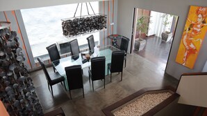 A modern dining area with a glass table and black chairs, a decorative hanging light fixture, and a view of the ocean through large windows. - The Bukit Ocean View Villa Jimbaran (Jimbaran)