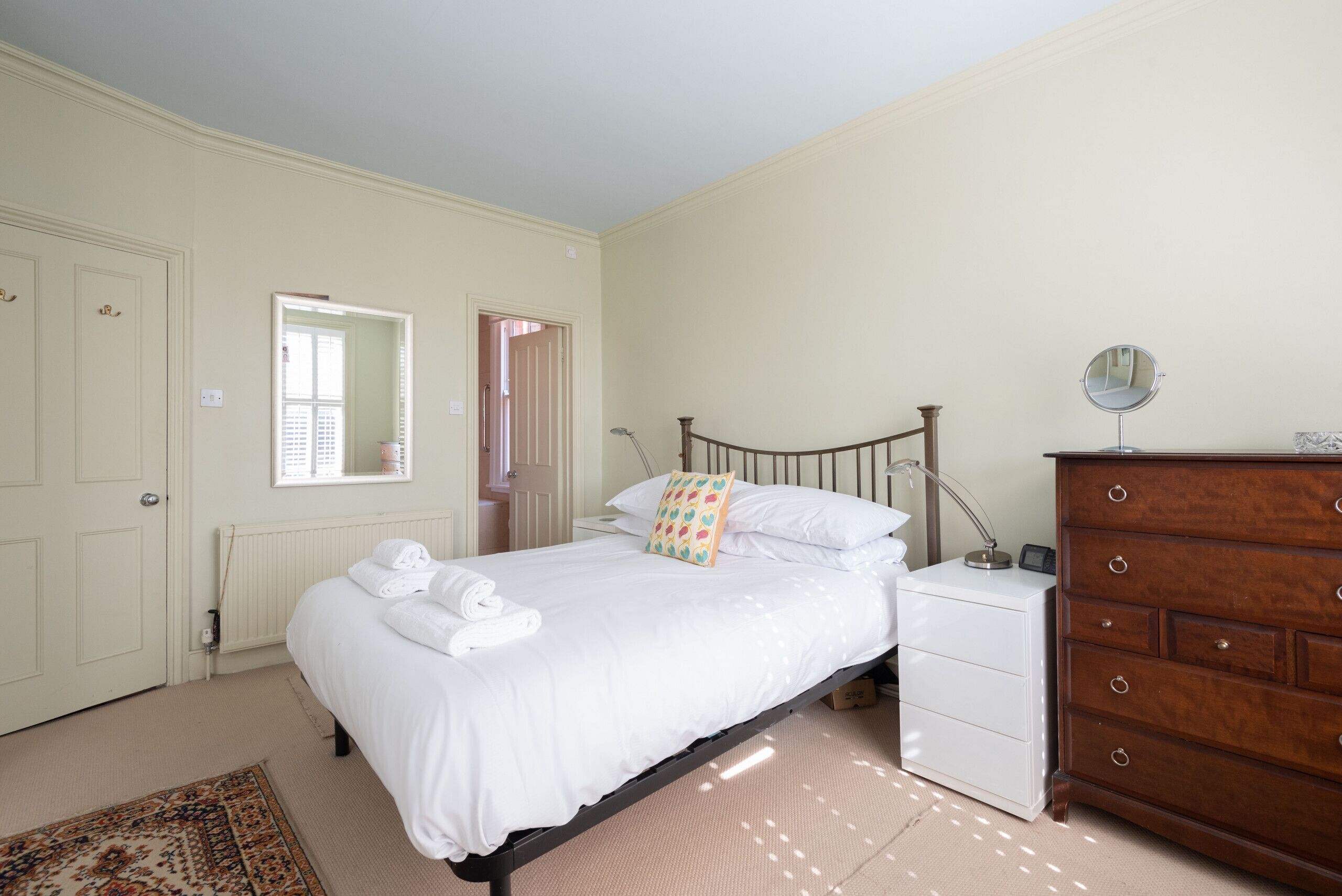 A bedroom with a bed, bedside table, dresser, and a mirror.