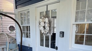 Une porte d’entrée ornée d’une guirlande décorative, un fauteuil suspendu et une petite table avec une plante.