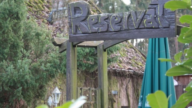 Un letrero de madera rústica con la palabra 'Reservas' grabada, sobre un fondo de follaje y una estructura de techo de paja.