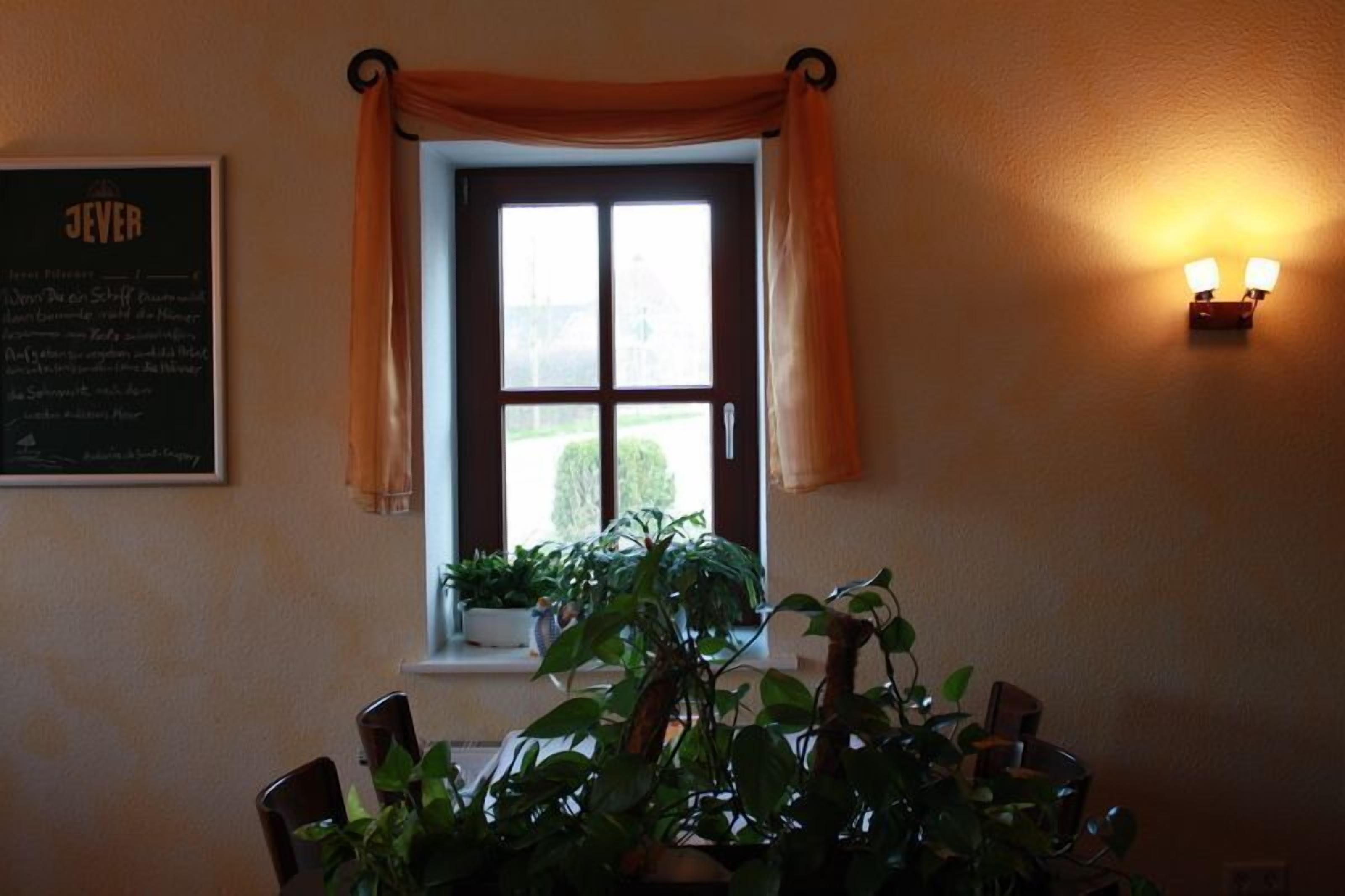 Zona pranzo con finestra, piante in vaso, lampada a parete e insegna incorniciata.