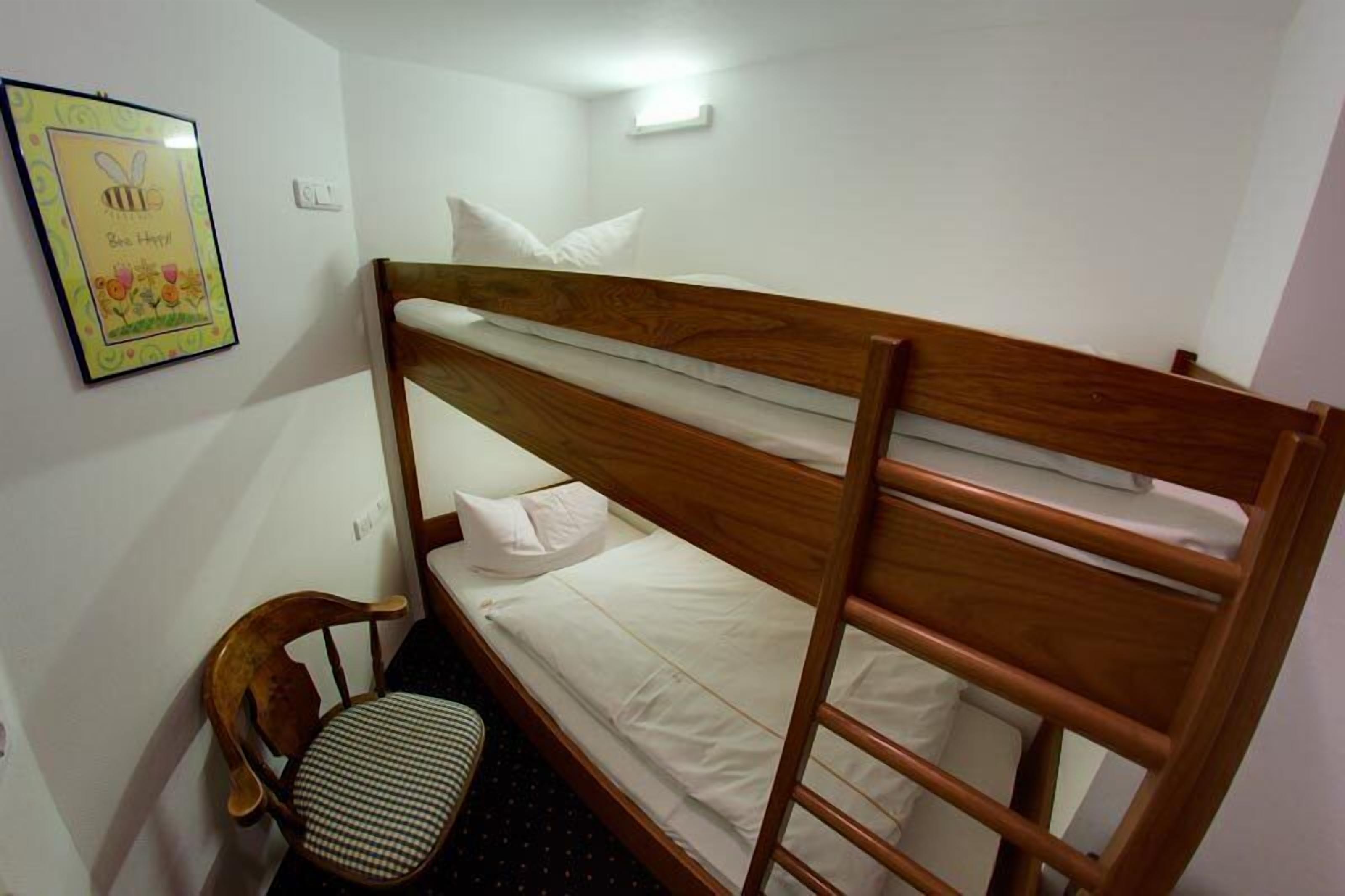 A bunk bed with white bedding, a wooden headboard, and a small chair with a checkered cushion.