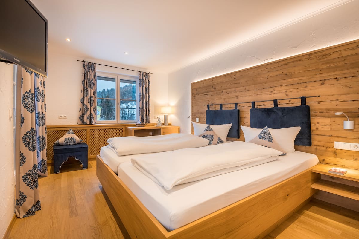 Una cama doble con cabecera de madera, una mesita de noche, una lámpara y una ventana con cortinas.