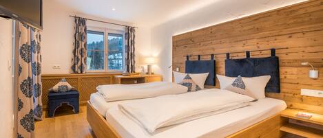 A double bed with a wooden headboard, a bedside table, a lamp, and a window with curtains.