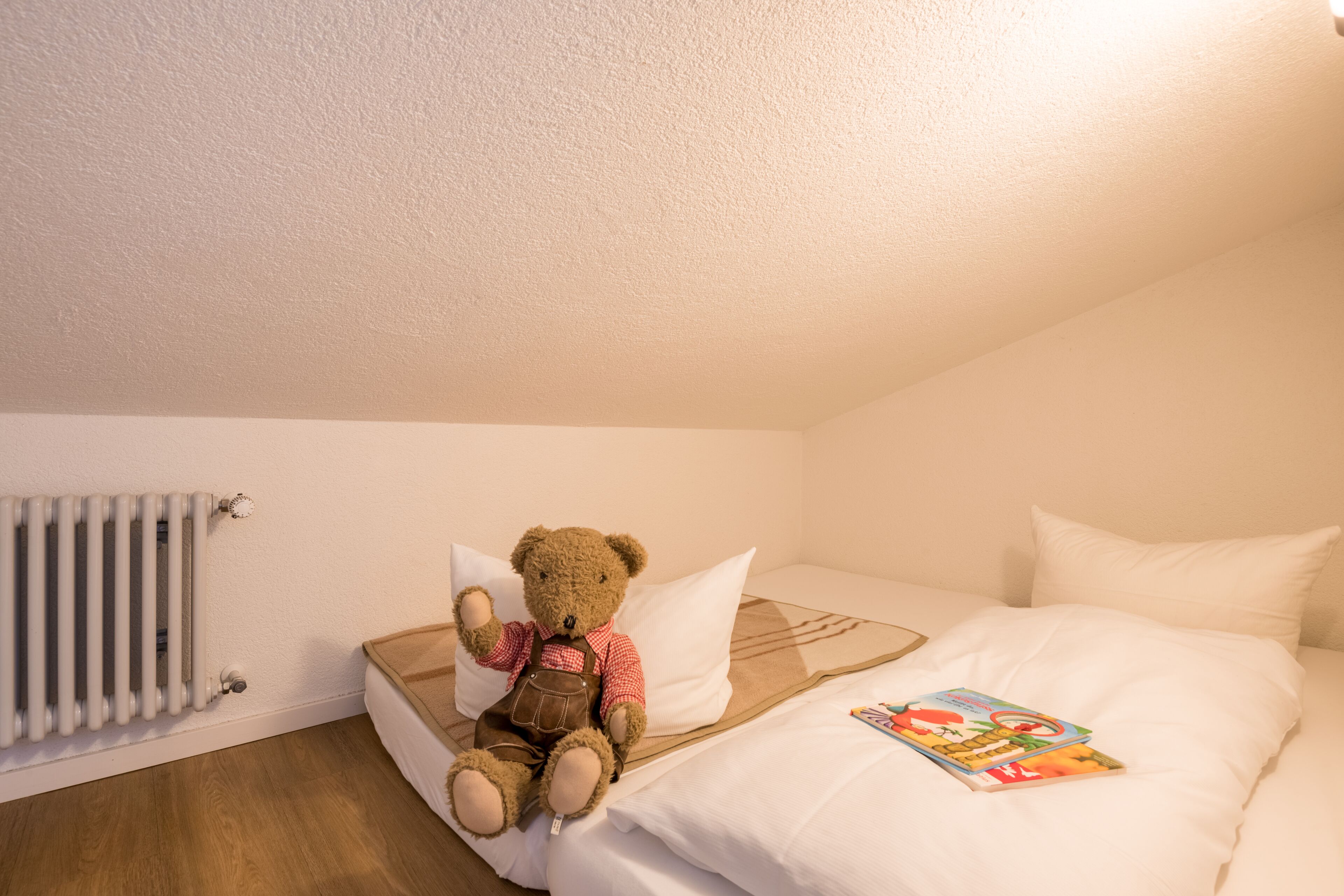 A cozy bedroom with a single bed, a teddy bear, and a book on the bed.