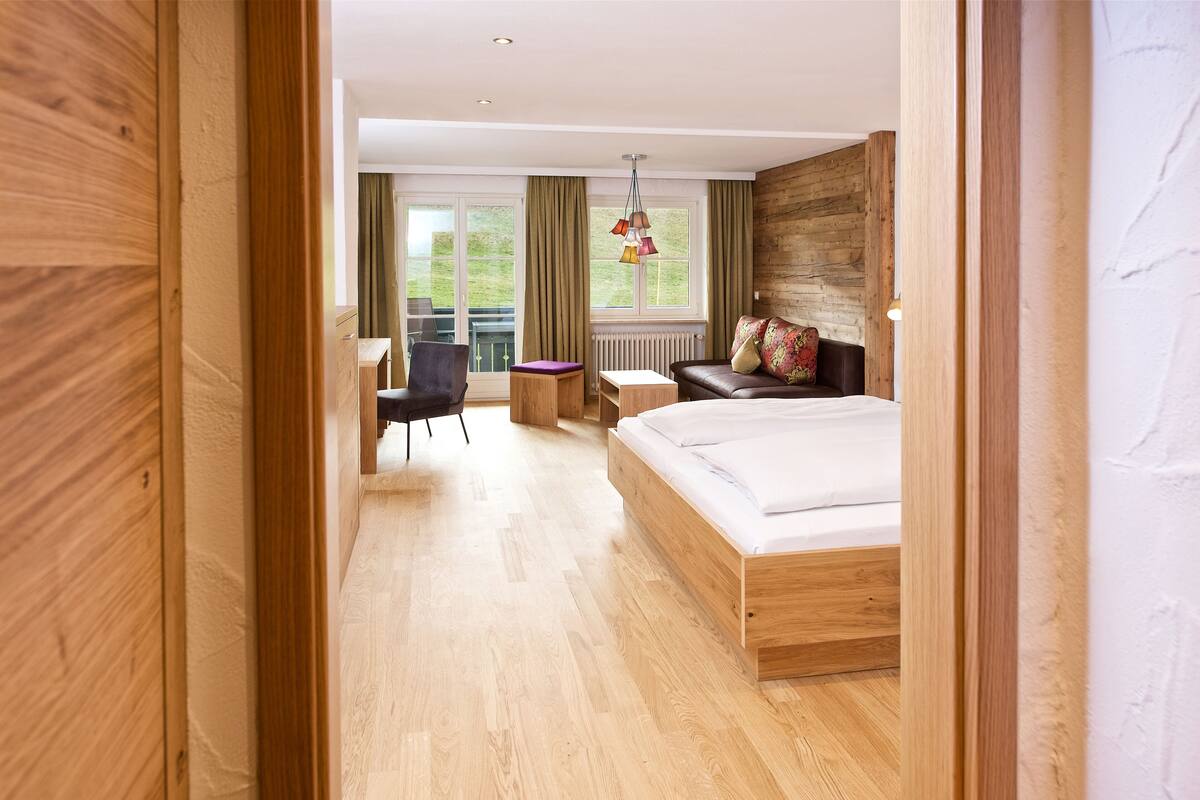 Una habitación de hotel moderna con una cama de madera, un escritorio, una silla y vistas al exterior.