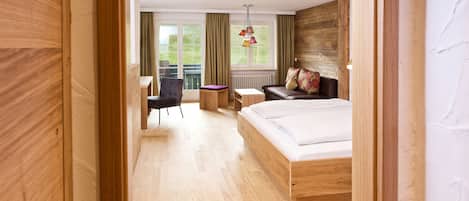 A modern hotel room with a wooden bed, a desk, a chair, and a view of the outdoors.